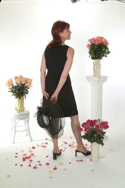 Model wearing Audrey Noir elegant black dress while holding hat